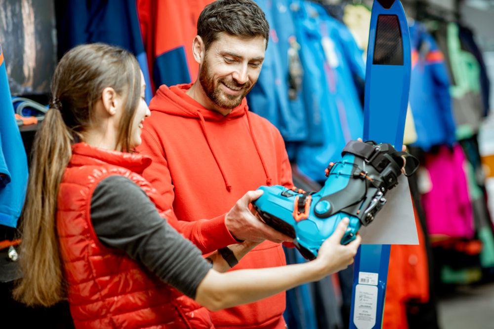 Verkäuferin zeigt Kunden unterschiedliche Modelle eines Skischuhes
